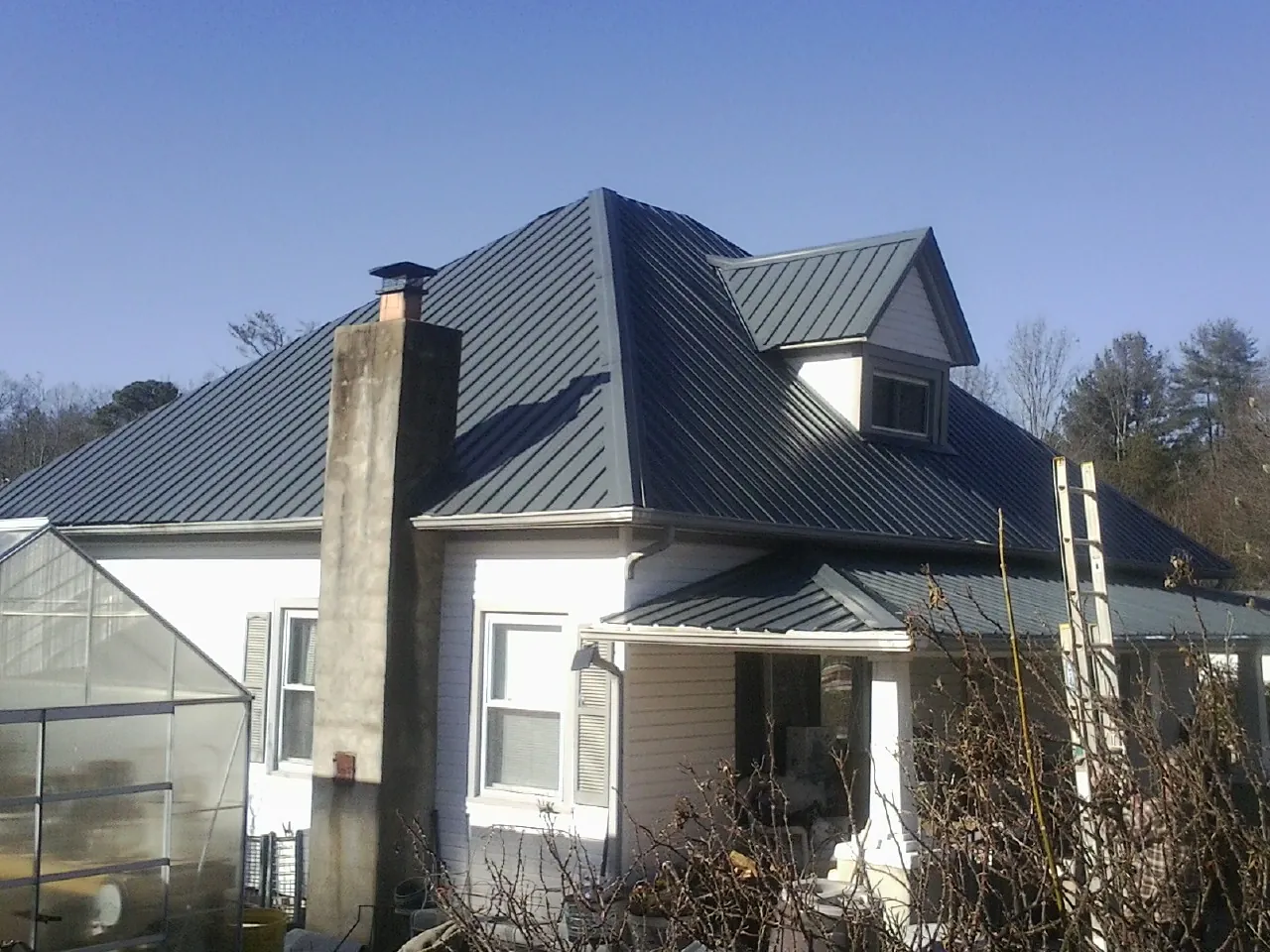 Dark blue standing seam metal roof on a white farmhouse with dormer — Slate & Tile Roof Repair by Roofing Brothers in Carnesville
