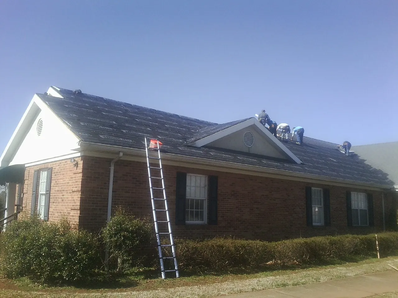 Crew tearing shingles off a brick ranch roof with a ladder set — Emergency Roof Repair work by our crew in Carnesville