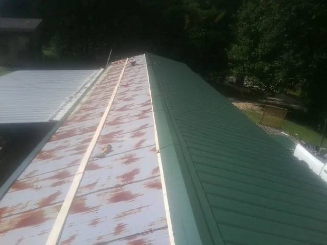 Old rusted panels beside newly installed green metal roofing — Wind Damage Roof Repair by Roofing Brothers in Carnesville