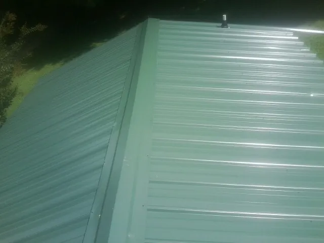 New green metal panels meeting at the ridge of a roof — Flat Roof Repair work by our crew in Carnesville