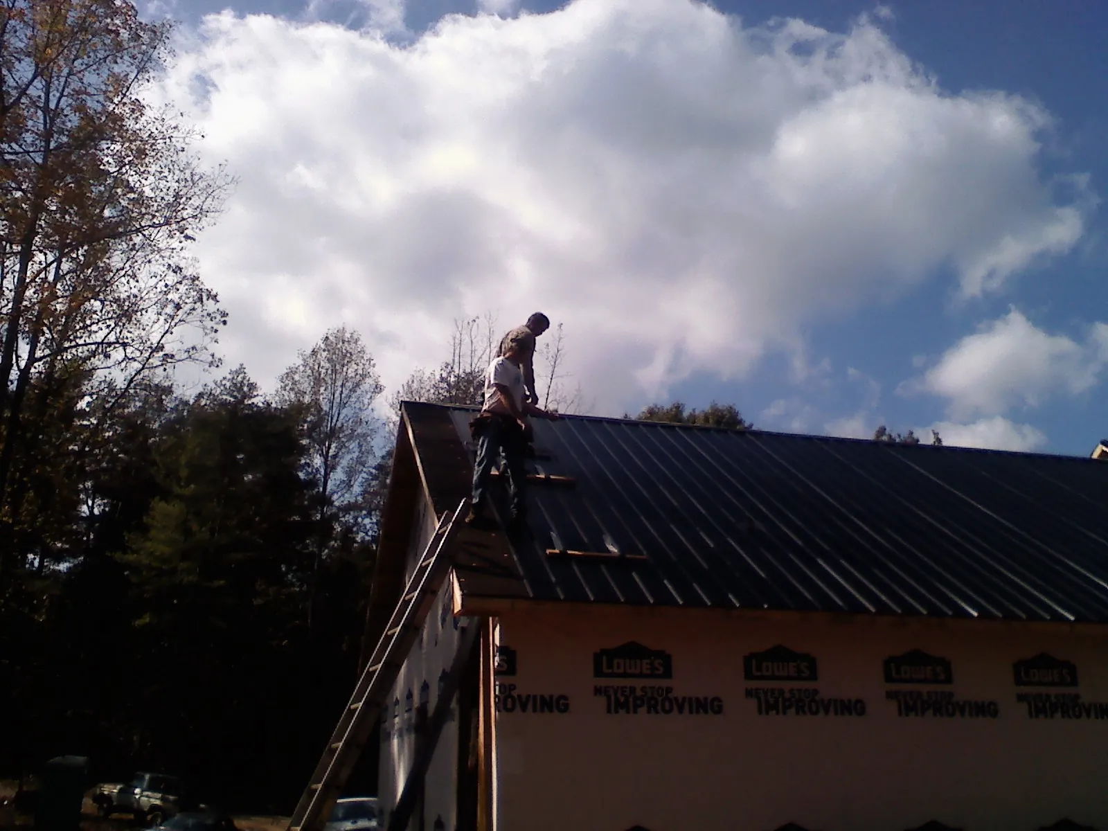 Roofer fastening dark metal panels high against a cloudy sky, from a Roof Inspection job in Carnesville