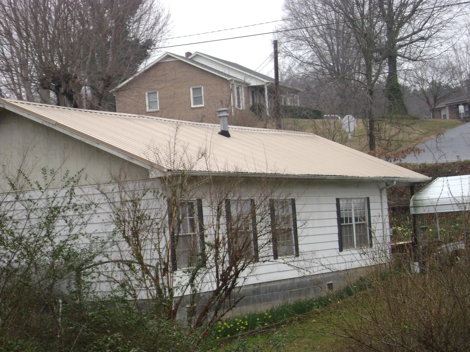 Tan metal roof on a white sided house set into a hillside — Commercial Roofing by Roofing Brothers in Carnesville